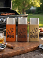 May include: Three rectangular metal cigar cases with leather-like sleeves in orange, brown, and tan. Each sleeve features a laser-engraved graphic of a cigar and a glass of whiskey with the text I'LL BE IN THE BACKYARD.
